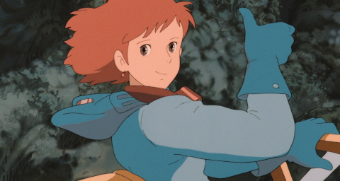 Nausicaä, her helmet and mask removed, which is dangerous in the situation she is in, her short red hair blowing in the wind. Nevertheless, she looks at the viewer with bright brown eyes, a smile, and a thumbs-up gesture.