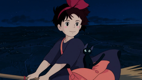 Kiki in a black dress with Jiji, her black cat, on a broom floats in the air over night fields dotted with the lights of small houses.