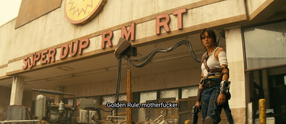 Lucy, one of the protagonists, in an iconic Fallout look: blue jumpsuit pulled down to look like pants, white tank top, a leather shoulder pad, Pip-Boy on her wrist, and a handgun in her hand. She is standing in front of a ruined Super-Duper Mart. The subtitle reads “Golder Rule, motherfucker.”