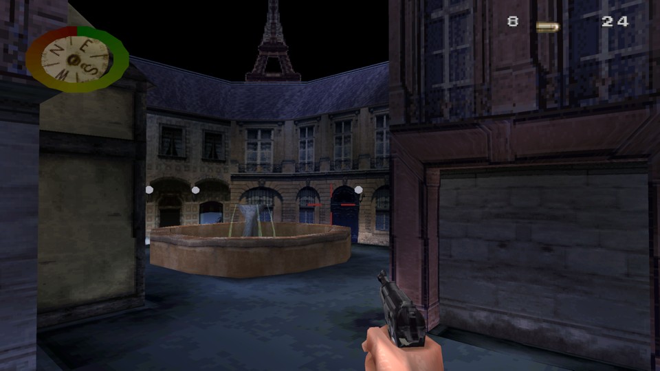 Small Parisian square with a fountain, surrounded by two and three story buildings. There is a pure black sky with the Eiffel Tower in the background. It is a first-person view with a hand of the protagonist holding a gun, a compass and a health circle in the upper left corner and an ammunition counter in the upper right corner.