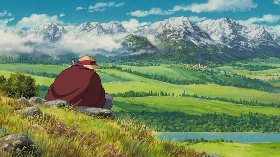 Sophie is sitting on some stones on a grassy hill. We only see her back, wearing a cloak and a straw hat. She is looking into the distance where there is a river with trees covering the bank, green fields and rolling hills separated by rows of trees. Far away, closer to snow-covered mountains under a blue sky with some fluffy clouds, is a city – only small dots of buildings.