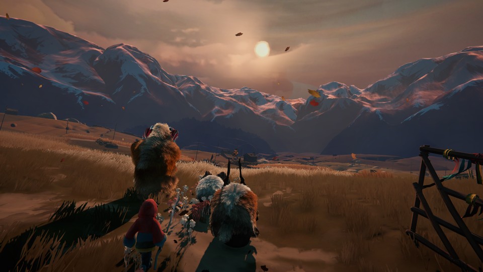 The protagonist, a human wearing a red jacket with blue and yellow accents, and holding a staff made of light wood, walks behind a small herd of fluffy, colorful bison/goat/sheep-like animals. They all walk on a green, grassy field. In the distance, there are a few human-made structures, such as wooden barns and telephone poles. Their destination is a range of snow-covered mountains under a warm setting sun.