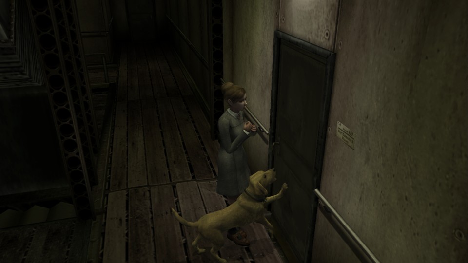 The dark, industrial-looking corridor has a floor of rough wooden planks, metal beams and handrails run alongside dirty walls. Jennifer, a young woman with dirt-blond hair in a bun, stands in front of a door. She wears a plain gray dress and holds her hands close to her chest. Beside her is her companion, Brown, a light brown Labrador retriever, who scratches at the door. The dark, industrial-looking corridor has a floor of rough wooden planks, metal beams and handrails run alongside dirty walls. Jennifer, a young woman with dirt-blond hair in a bun, stands in front of a door. She wears a plain gray dress and holds her hands close to her chest. Beside her is her companion, Brown, a light brown Labrador retriever, who scratches at the door.
