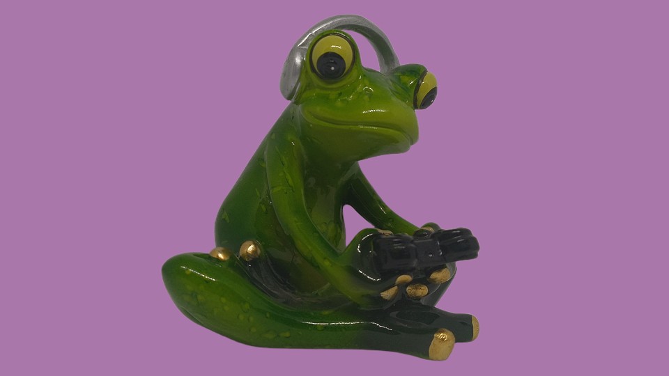 A ceramic frog. It’s slightly anthropomorphic and a bit cartoonish, mostly because it sits cross-legged, holds a black gamepad, and wears silver over-the-ear headphones.
